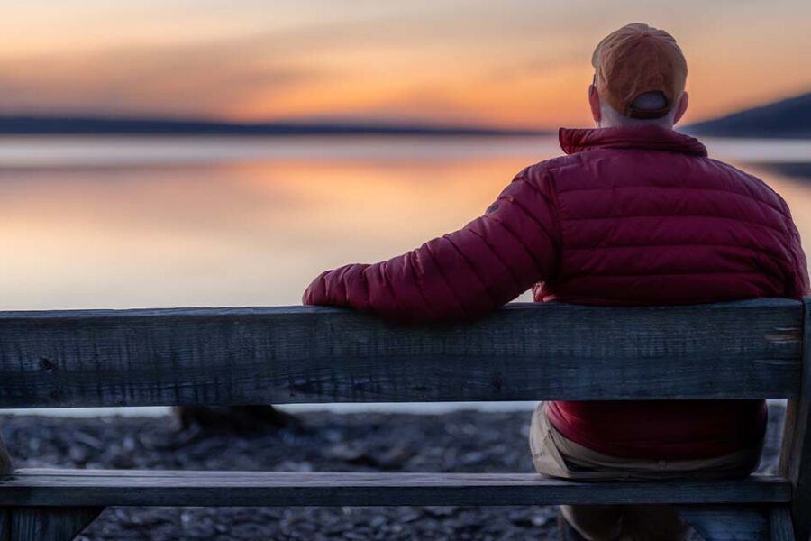 back of man sitting on bench looking out at the lake